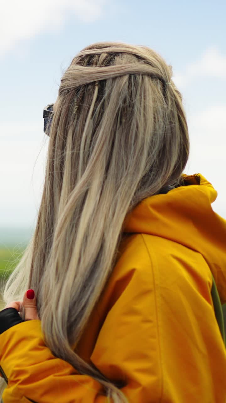 Mujer joven con chaqueta amarilla y gafas de sol mirando el paisaje