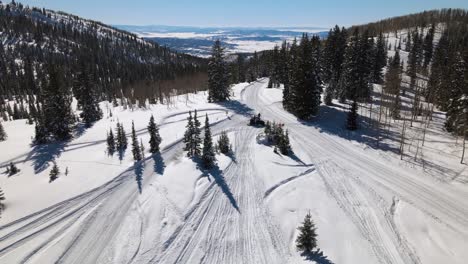 Excellent-Aerial-View-Of-A-Man-Parked-On-A-Snowmobile-Amidst-Pine-Trees-On-A-Mountain