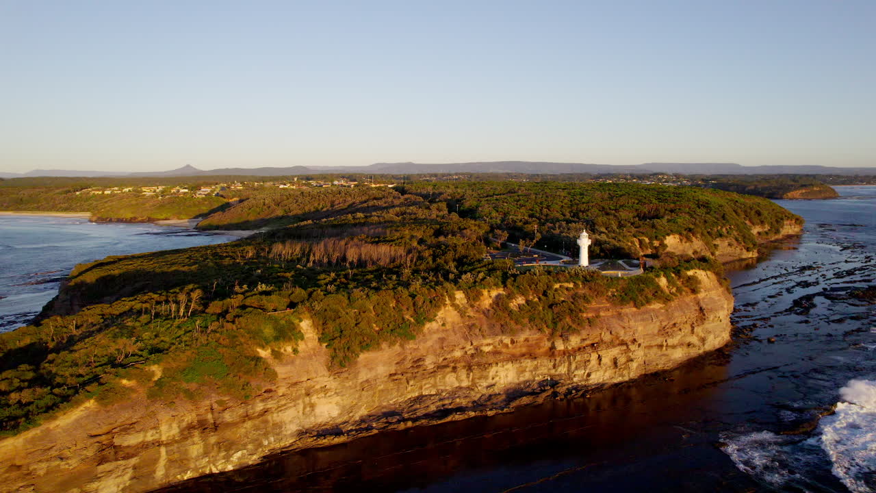 Warden Head Lighthouse stands proudly above rugged cliffs as waves crash far below. Framed by morning light, this coastal sentinel overlooks the vast, blue Tasman Sea near Ulladulla, NSW, Australia.