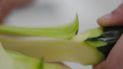 Handheld-approaching-hands-slicing-cucumber-with-vegetable-peeler