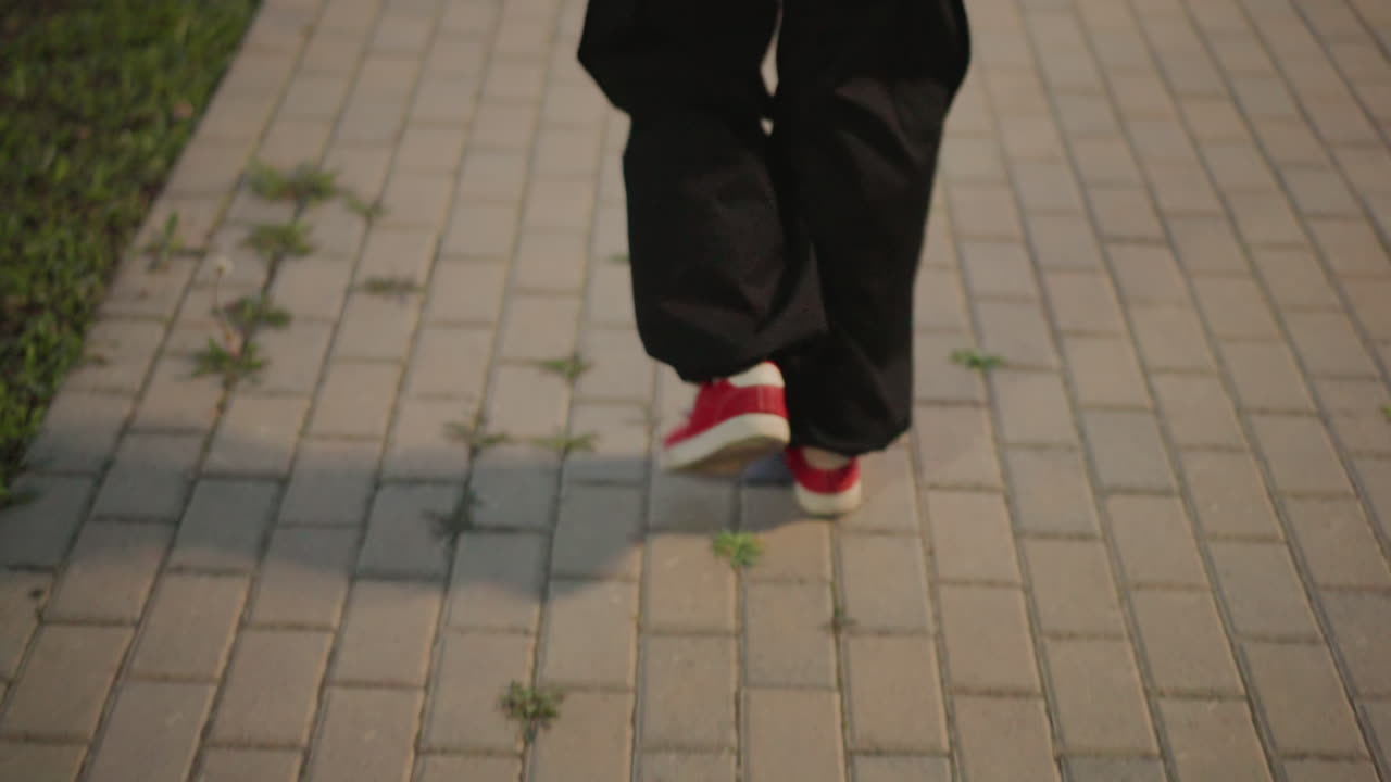 akşam vakti şehirde yapılan, ayak hareketlerine odaklı bir prova; fayanslı yolda güçlü adımlar, lamba ışığı altında eğitim yapan tek bir performans sanatçısı, uzun gölgeler, sıcak sinematik tonlar, disiplinli ritim ve azim