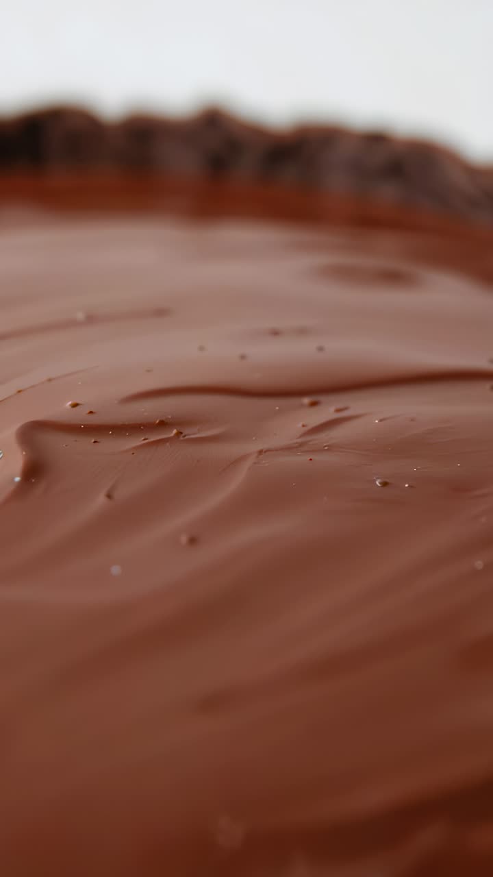 Vertical video: Shifting camera showcasing ganache tart fluted crust bubbles settling on tabletop