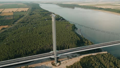 braila bridge supporting tower with flashing obstacle lights in daytime. danube river with dense green forest and agricultural fields in romania. drone shot