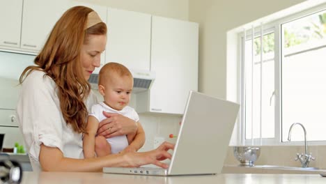Beautiful-brunette-using-laptop-and-holding-her-baby-daughter