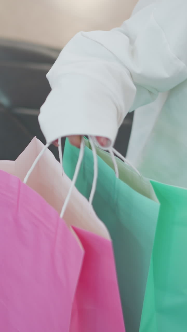 vista parcial de una mujer con un traje blanco colocando bolsas de compras rosas y menta en un asiento de cuero en un centro comercial se sienta cerca de ella mientras coloca su mano en su regazo con un fondo borroso