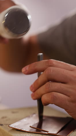 worker taps punch tool with hammer to make holes in leather workpiece at table in workshop closeup. traditional accessory craft technology