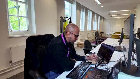 A-businessman-wears-glasses-and-works-on-his-stylus-on-smartphone-at-his-desk-in-a-brightly-lit,-modern-office-environment