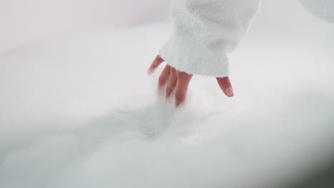 woman dips fingers into thick bubble bath closeup. young lady gently touches foam preparing for spa relaxation procedures at home. weekend relax ritual