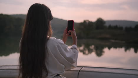 woman taking picture at sunset by the lake