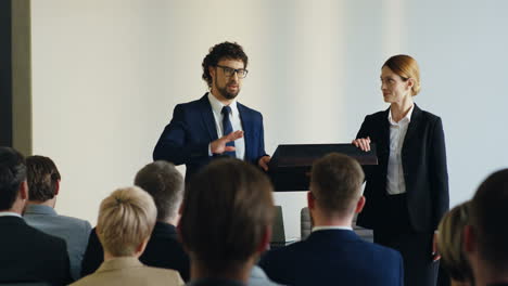 empresaria caucásica y hombre de negocios en un podio frente al auditorio y presentando un proyecto en una conferencia