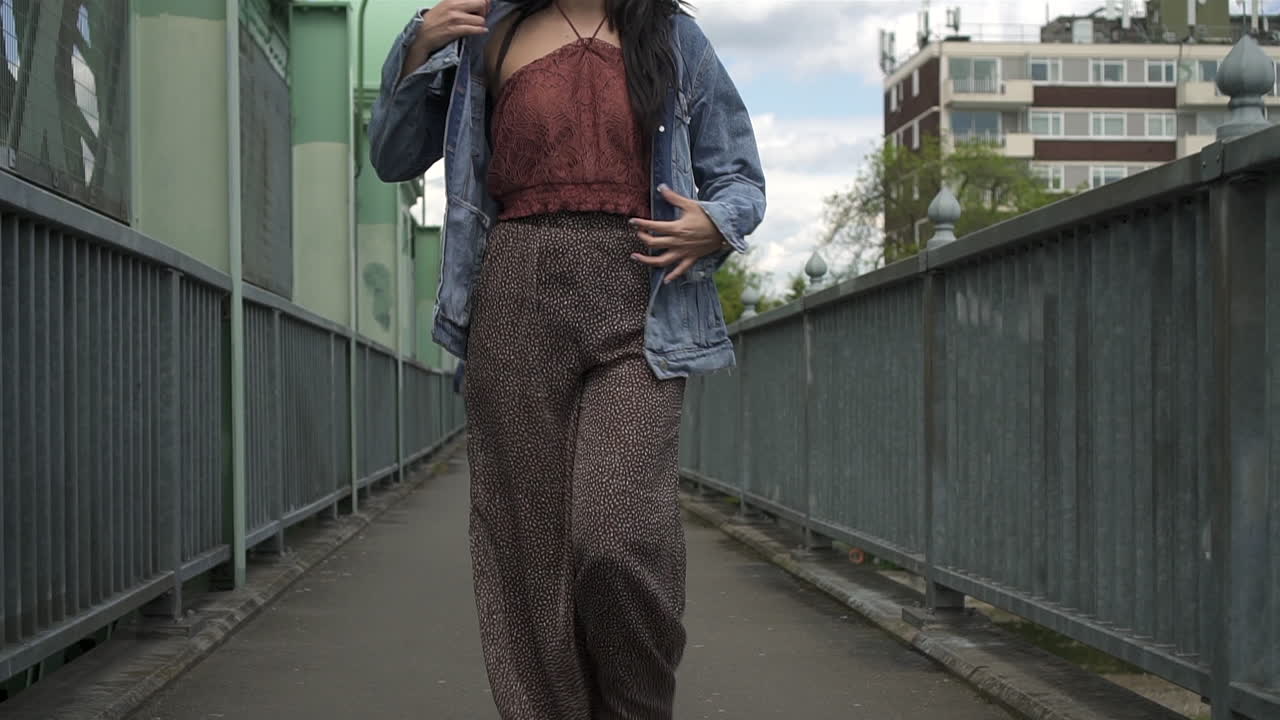 그녀의 데님 재킷을 벗고 모델링하고 카메라를 향해 걸어가는 동안 화려한 히스패닉 갈색 머리를 기울입니다.