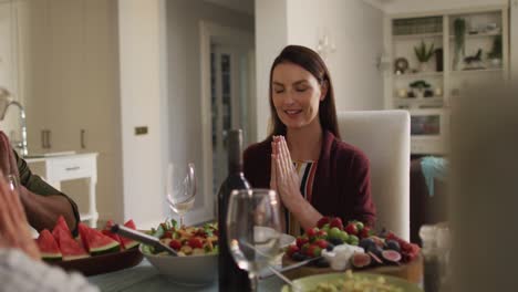 madre caucásica sonriente sentada en la mesa en oración antes de la comida familiar