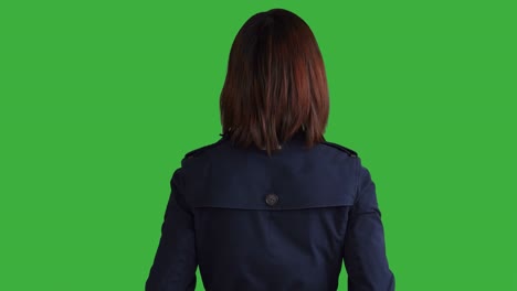 young asian woman wearing a blue coat. using smartphone, digital tablet and looking at camera. woman standing in front of a green screen for chroma key.