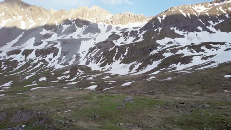 Aerial-drone-footage-flying-forward-and-close-to-an-alpine-meadow-in-a-dramatic,-jagged-mountain-landscape-with-residual-patches-of-snow-and-alpine-meadows-in-Switzerland