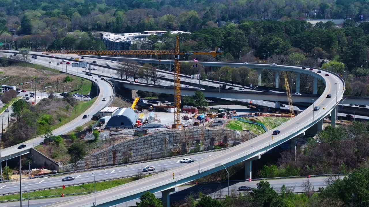 Interstate traffic and elevated highway during sunny day in Atlanta Suburb. Aerial wide shot. Yellow crane on construction site. Spring day in USA.