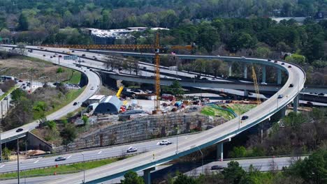 interstate traffic and elevated highway during sunny day in atlanta suburb. aerial wide shot. yellow crane on construction site. spring day in usa.
