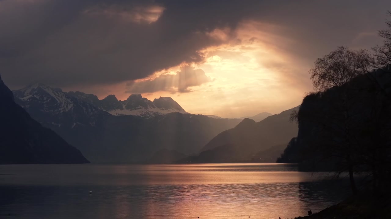 Golden sunset light breaks through dramatic clouds above Walensee in Switzerland. Sun rays illuminate the lake and surrounding alpine peaks, creating a breathtaking evening atmosphere.