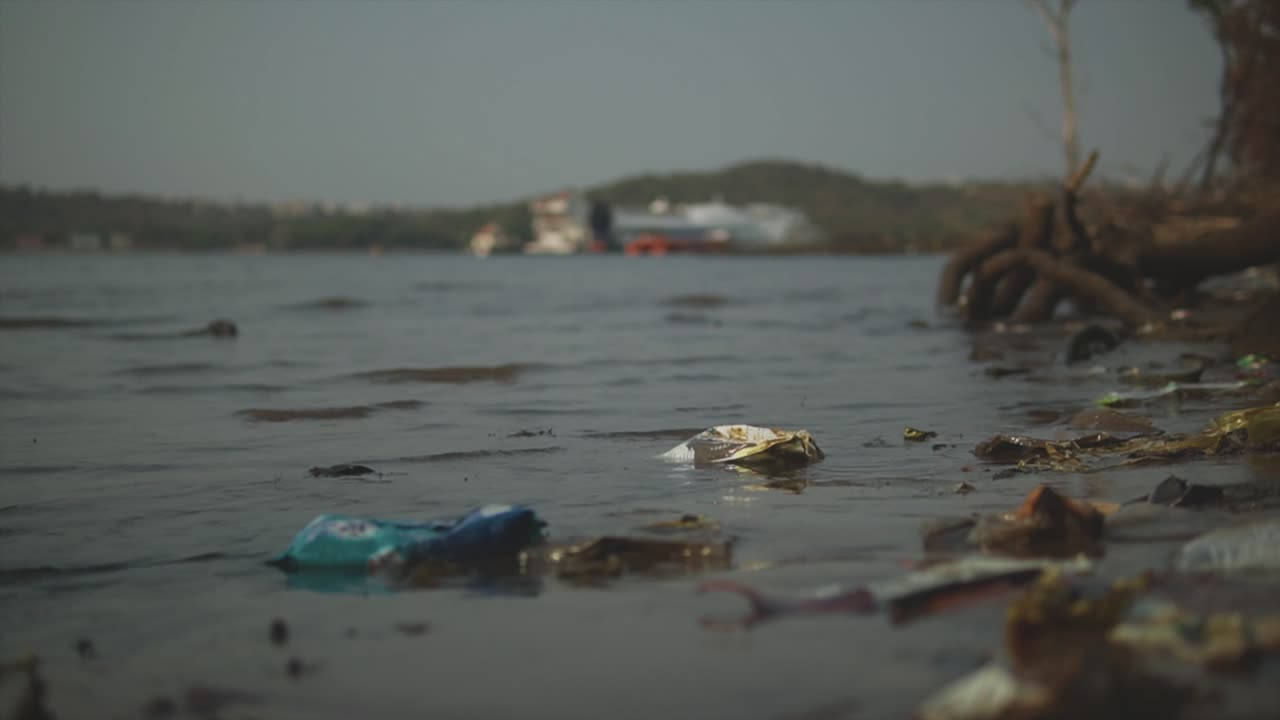un primer plano de las ondas empujando hacia la orilla contaminada del río mandovi, la orilla cubierta de basura y basura, panjim, india