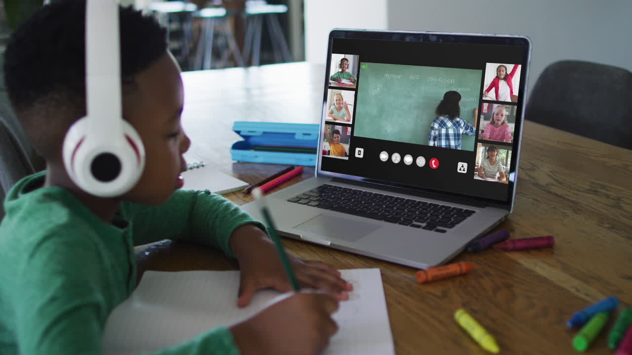 Schoolboy using laptop for online lesson at home, with diverse teacher and class on screen