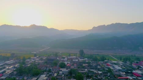 fotografía aérea del sol que se levanta sobre las montañas con un pequeño pueblo en primer plano