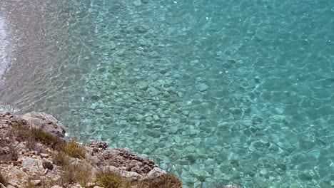 Bahía-Tranquila-En-La-Costa-Mediterránea-Con-Una-Hermosa-Playa-Y-Acantilados-Sobre-Agua-De-Mar-Limpia-Y-Color-Turquesa.