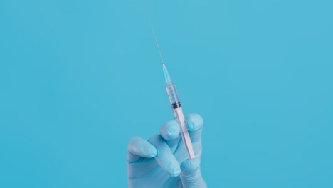 syringe in a gloved hand against a blue background