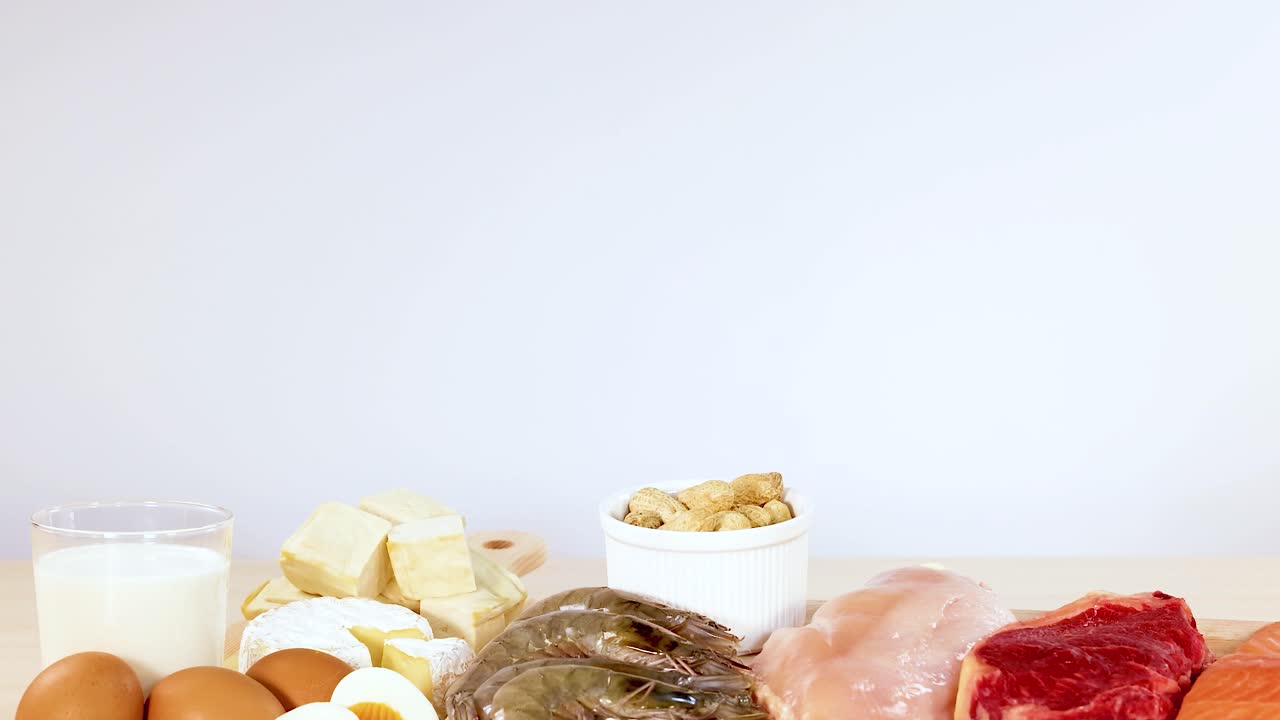En række proteinrige fødevarer, herunder kød, skaldyr, mejeriprodukter og nødder, er pænt arrangeret på et bord.