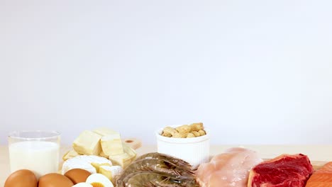 una variedad de alimentos ricos en proteínas, incluidas carnes, mariscos, lácteos y nueces, están ordenadamente dispuestos en una mesa