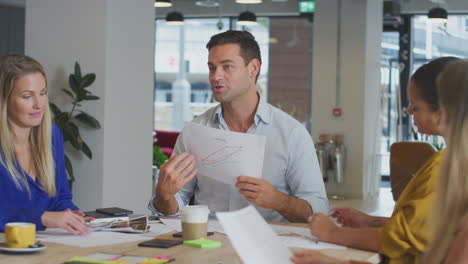 business team having meeting sitting around table discussing document in modern open plan office