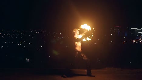 young blond bare-chested male spins two burning pois slow motion shot