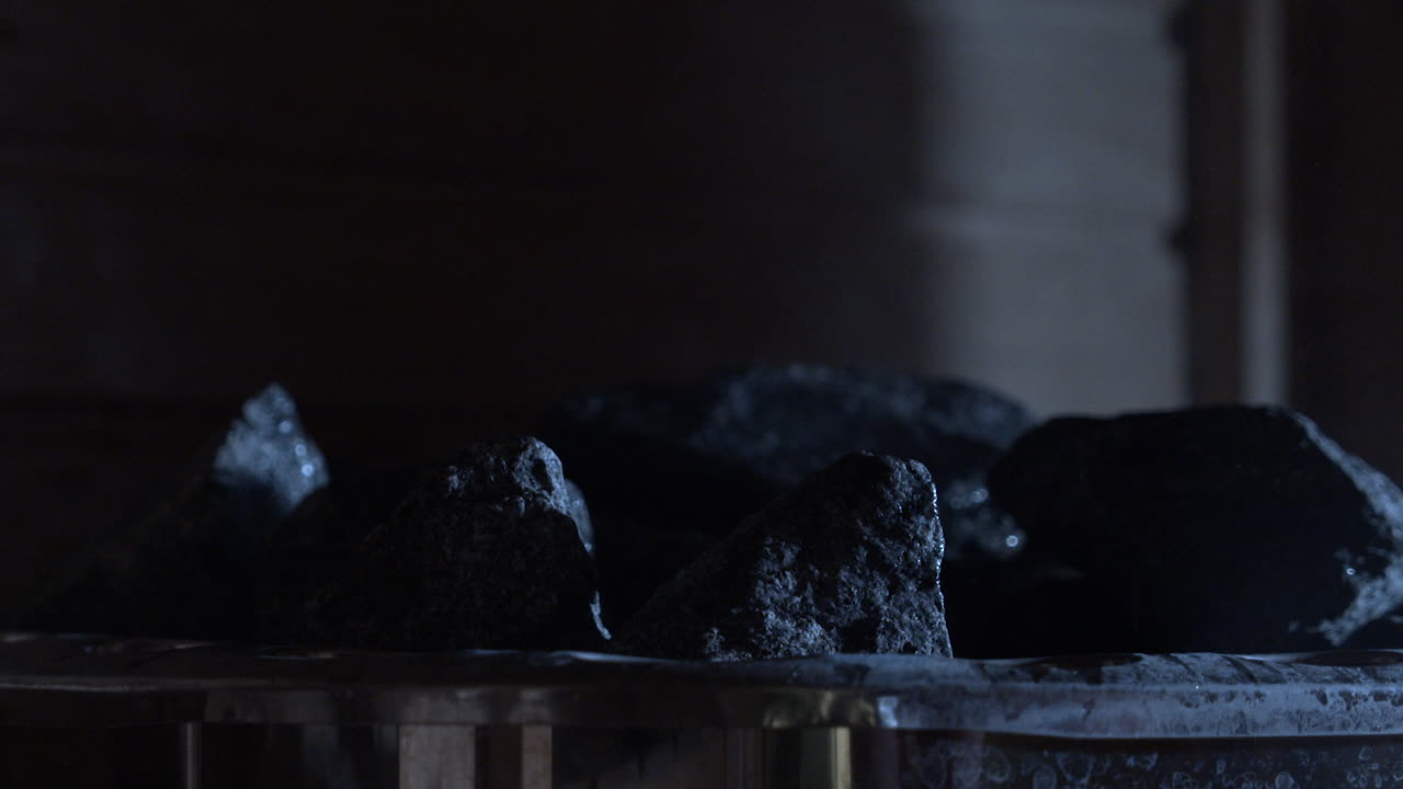 льет воду на распаренные камни в финской сауне, снимок крупным планом