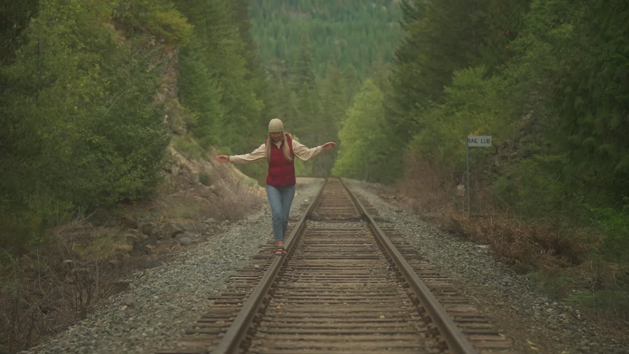 Donna hipster dallo spirito libero in equilibrio su un binario ferroviario in acciaio abbandonato
