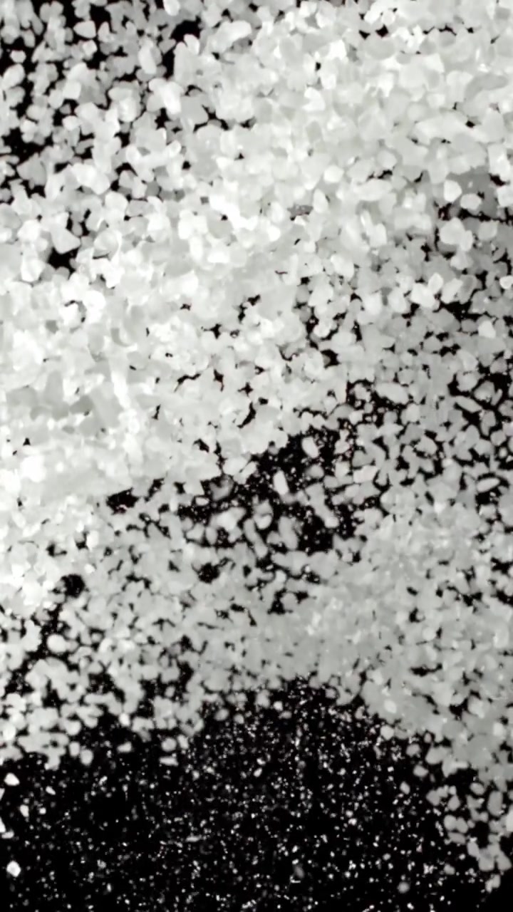 Cristalli di sale bianco che cadono e si spargono su uno sfondo nero