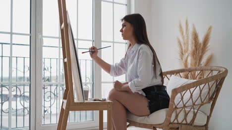 lady draws picture on canvas sitting in rattan armchair