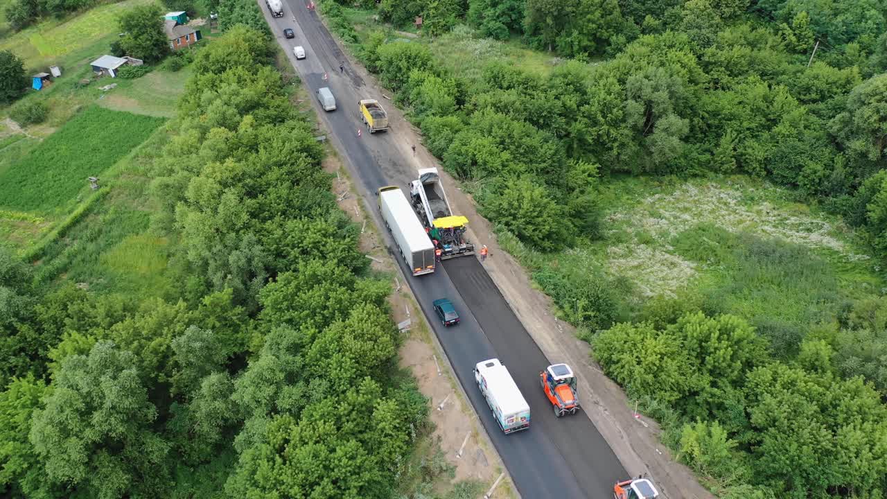 Roadworks on the highway. Trucks and cars passing near the road construction site in summer. Aerial view. Camera moves top down.