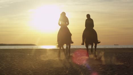 silueta de dos mujeres jóvenes montando caballos en la playa