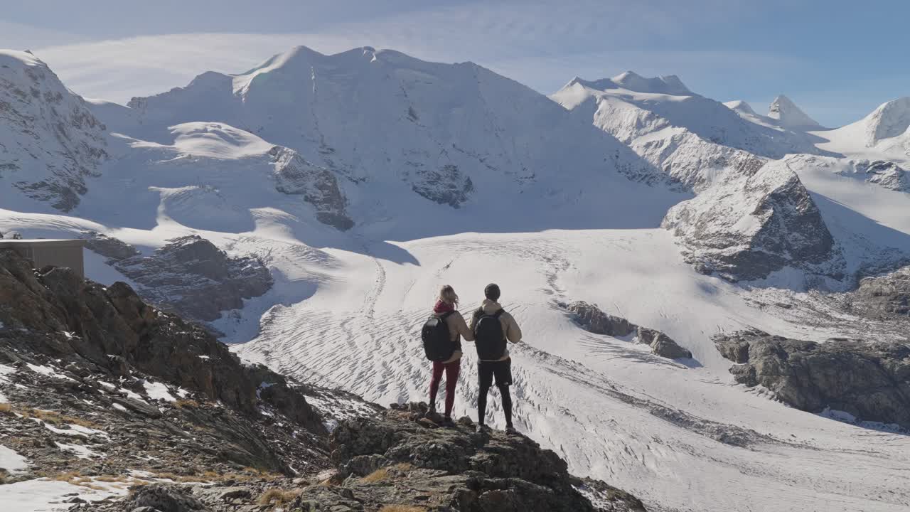 Adventure couple reaching viewpoint overlooking large glacier in Alps
