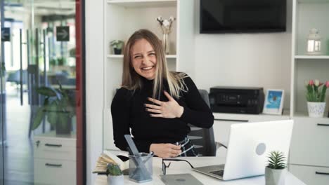 la joven rubia está sentada en un escritorio y comienza a reír muy sinceramente