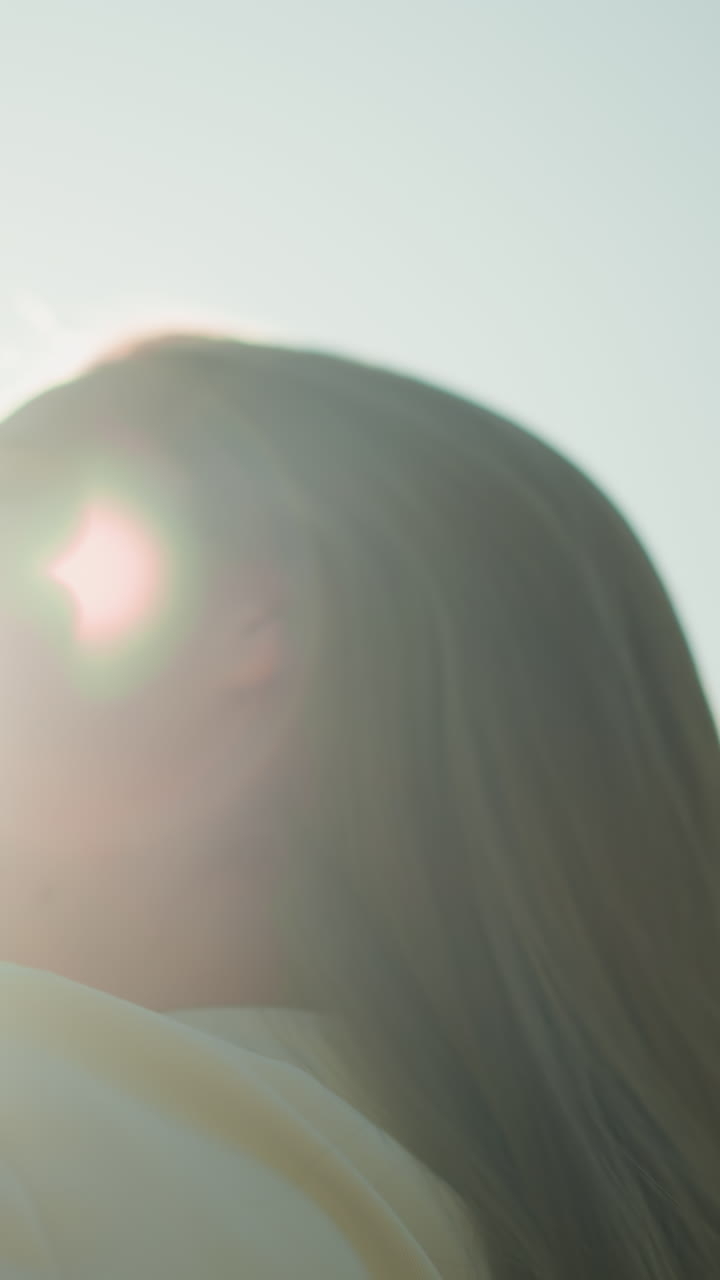 검은 장갑을 입은 여자는 머리를 뒤로 기울여, 은 빛이 그녀의 얼굴을 둘러싸고 빛나는 빛을 일으키면서 그녀의 흐르는 머리카락을 조정합니다.