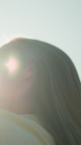 dama con guantes negros inclina la cabeza hacia atrás, ajustando su cabello que fluye como la cálida luz del sol crea un resplandor radiante alrededor de su cara, árboles verdes suavemente borrosos y follaje