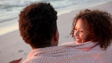 biracial couple enjoys a sunset at the beach, the woman with curly hair smiling warmly