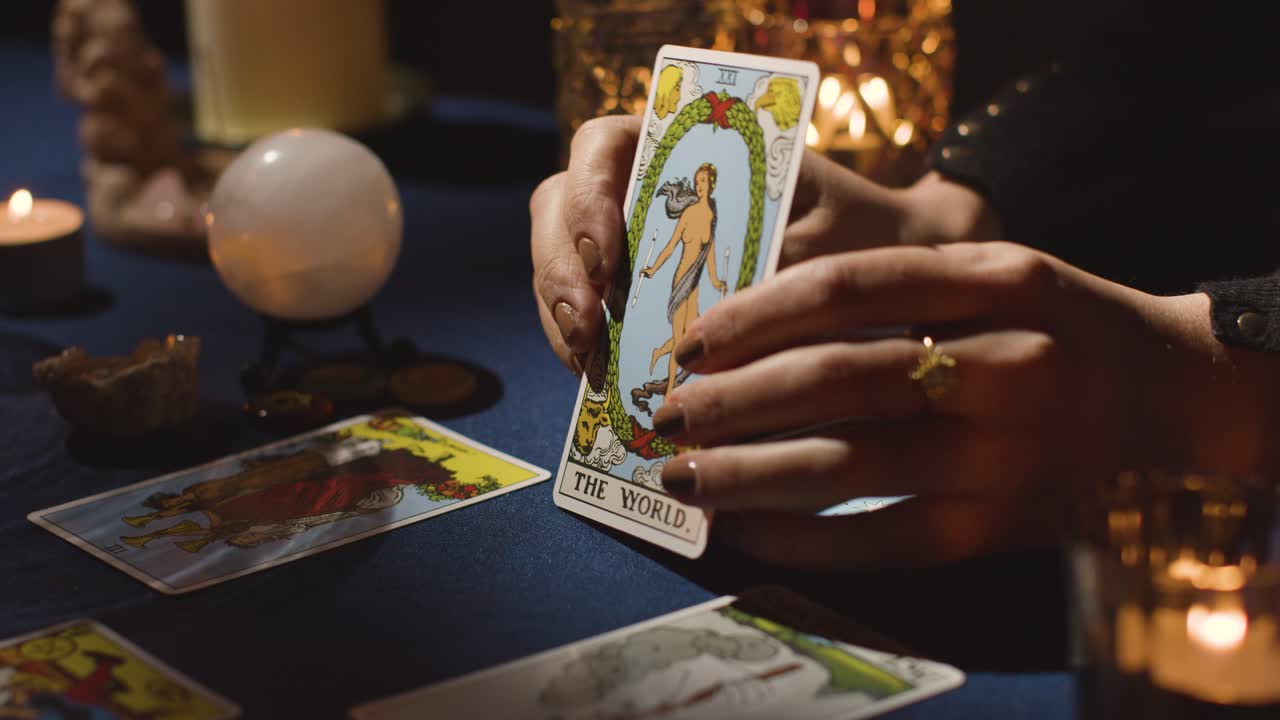 primer plano de una mujer dando una lectura de cartas del tarot en una mesa a la luz de las velas sosteniendo la carta del mundo 2
