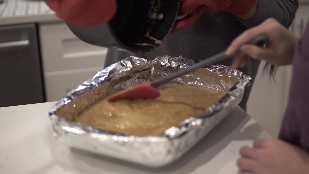 Mor og datter hælder en karamelblanding på en bund til millionær shortbread-kager.