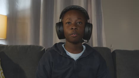 boy at home sitting on sofa wearing headset playing video game