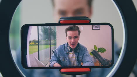 male vlogger wearing headphones with microphone live streaming on mobile phone