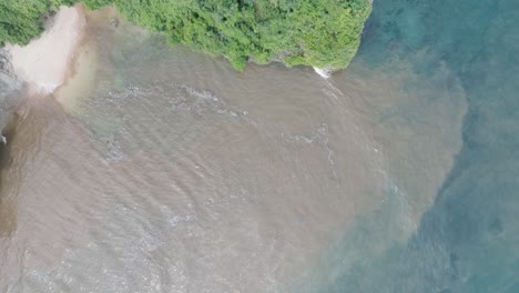 Top-down-aerial-drone-shot-over-polluted-sewage-water-and-floating-trash-with-debris-over-dead-coral-reef-mixing-with-turquoise-water-and-tropical-coastine-in-Bali-Indonesia