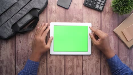persona usando una tableta con una pantalla verde en una mesa de madera