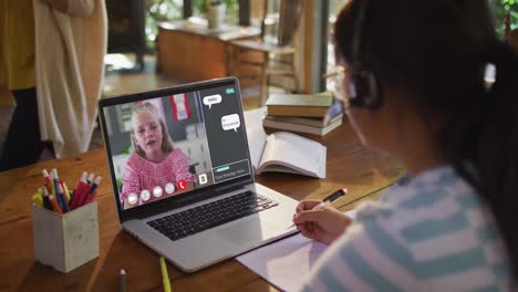 Schoolgirl-using-laptop-for-online-lesson-at-home,-with-girl-talking-and-web-chat-on-screen