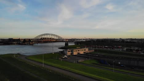 drone pan shot of vehicles driving into a tunnel underneath a river while cars driving on a bridge above the water on a partly cloudy day during golden hour on a winter day in the netherlands