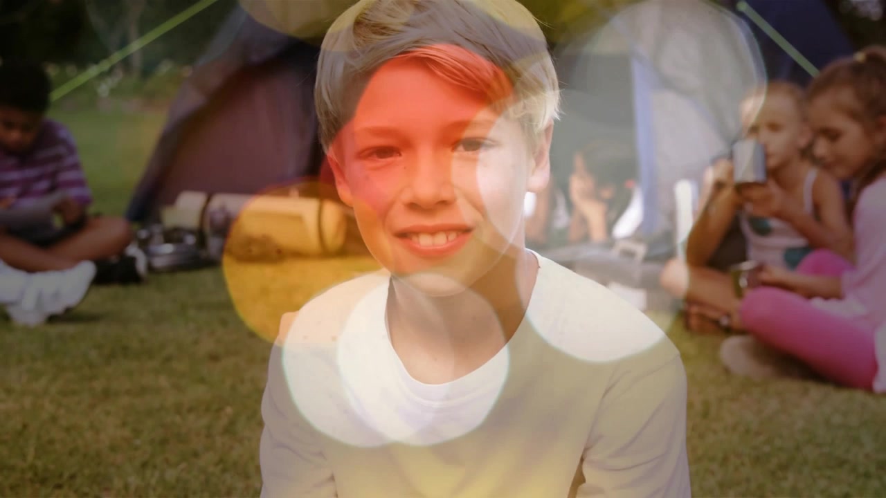 Blond boy sitting near tent, bokeh overlay drifting over device, coloring faces, boosting camp mood